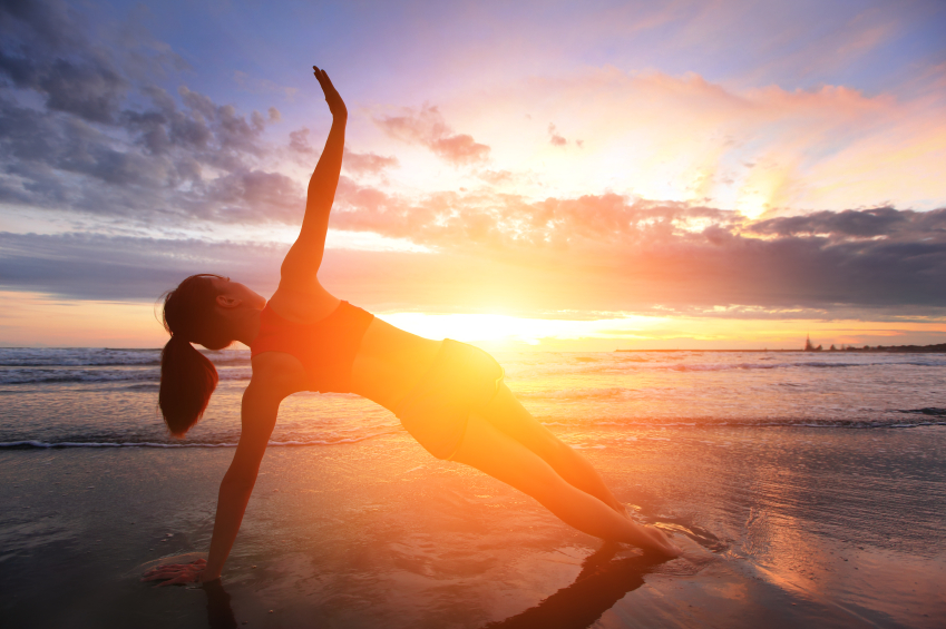 Sport Young woman silhouette practicing yoga on the sea beach at sunset